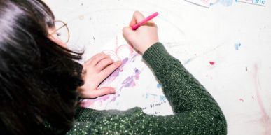 Man sieht einer Frau mit grünem Pullover über die Schulter. Die Frau arbeitet und hat einen Stift in der Hand.