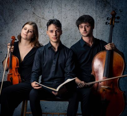 Drei Personen sind elegant gekleidet und schauen in die Kamera. Eine Person mit Violine, eine mit Notenbuch und eine mit Cello.