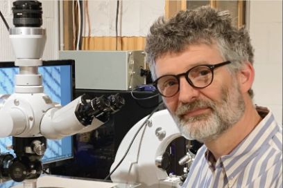 Portrait von Professor Sebastian Dobrusskin, der neben einem Mikroskop sitzt.