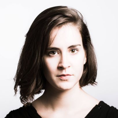 Portrait of a young woman with shoulder-length hair against a light grey background.
