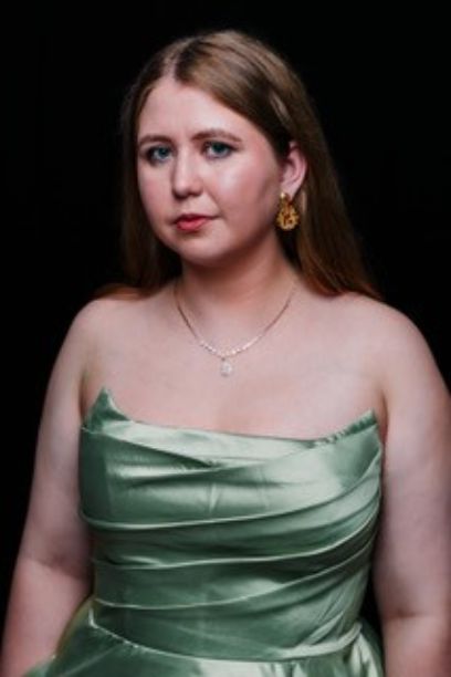 Frontales Portrait einer braunhaarigen Frau in einem glänzenden hellgrünen Kleid. Sie trägt Ohrringe und eine Silberkette,