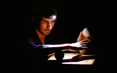 Mann mit Stirnlampe an Tisch mit Jonglierball in der Hand
