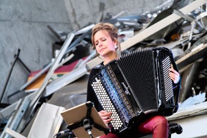 Viviane Chassot sitzt vor Metallschrott und spielt Akkordeon.