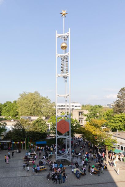 Sicht auf den Platz mit dem Glockenturm. Darunter sind runherum Tische aufgestellt und viele Menschen zu sehen.