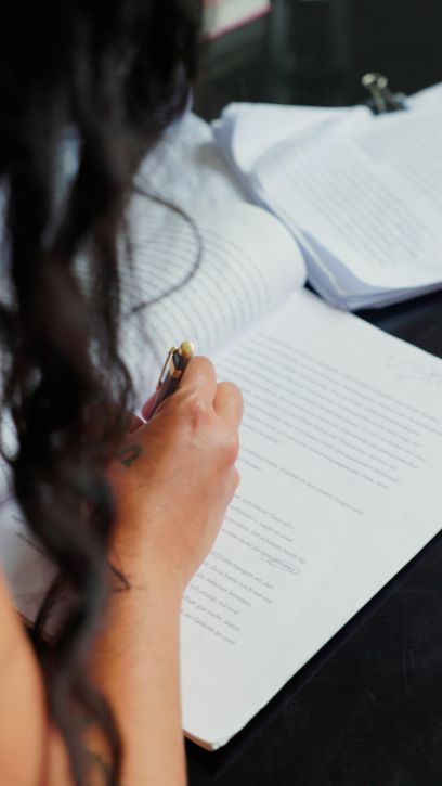 Vue par-dessus l'épaule, jeune femme travaillant sur un manuscrit imprimé, un stylo noir à la main