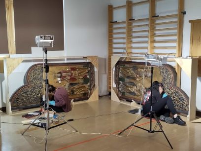 Rückwand eines Altars wird von zwei jungen Menschen bearbeitet, Lichter im Vordergrund, im Hintergrund eine Sprossenwand einer Turnhalle