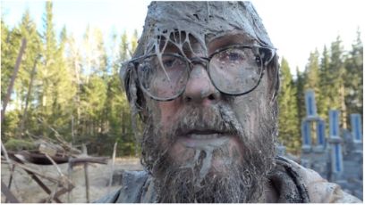 Portrait von Trond Reinholdsten in einem Wald, er trägt Brille und Bart, das ganze Gesicht ist mit Schlamm verschmiert