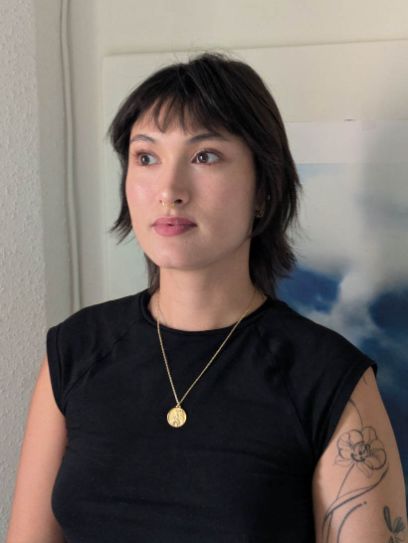 Eine Frau schaut links an der Kamera vorbei. Sie trägt ein schwarzes Kleid und eine goldene Halskette.