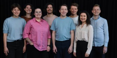 Acht Personen schauen direkt in die Kamera. Sie stehen vor einem schwarzen Hintergrund.