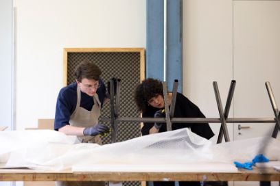 Ein junger Mann und eine junge Frau arbeiten an einer Metallkonstruktion mit Pinseln.