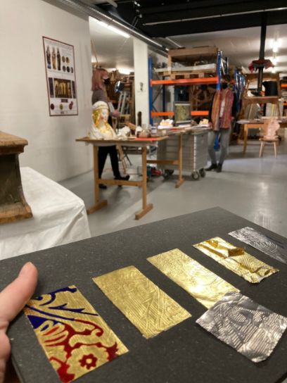 Aufnahme aus einem Atelier. Goldige Papiere auf dunklem Tisch im Vordergrund.