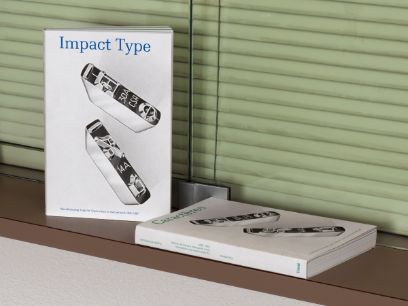 Auf einem Fenstersims vor grünem Rollladen steht ein Buch "Impact Type", daneben eine Ausgabe liegend