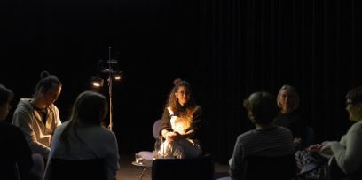 Christoph Jenny, Tina Schück und Carla Helmrich (von links nach rechts) sitzen auf breiten Stühlen und diskutieren mit dem Publikum. In der Mitte hat es eine Stehlampe die Licht spendet, sonst ist es ein dunkler Raum.