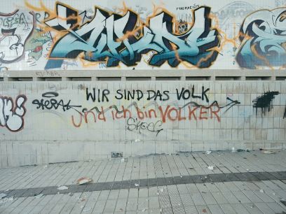 Eine graue Wand mit diversen Grafittis. In der Mitte steht «Wir sind das Volk» und unten in anderer Schrift «und ich bin Volker».