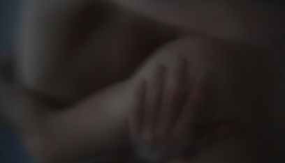 Ein abgedunkeltes, unscharfes Bild zeigt ineinander verschlungen eine Hand, einen Arm und einen Oberkörper.