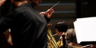 Aufnahme durch ein Blasmusikorchester, die eine Hand mit Dirigentenstab zeigt.