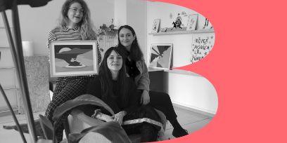 Schwarz-weiss-Aufnahme von drei Frauen in einem Studio sitzend, in die Kamera schauend mit einem Gemälde in der Hand.