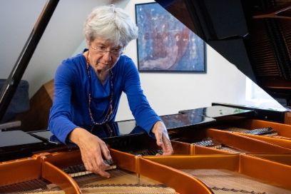 Katharina Weber steht über einen geöffneten Flügel gebeugt und zupft die Klaviersaiten.