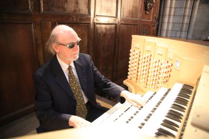 Ein Mann mit Sonnenbrille sitzt am hell erleuchteten Orgelspieltisch der Kirche Notre Dame in Paris und hat die Hände auf den Tasten.