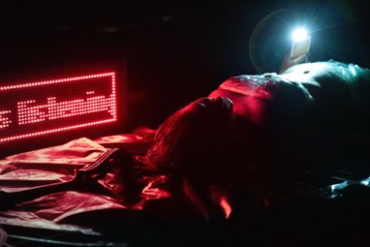 Eine Frau liegt rot angestrahlt auf der Bühne, links im Hintergrund ist eine Anzeige «listening» zu sehen, rechts im Hintergrund das Licht eines Scheinwerfers