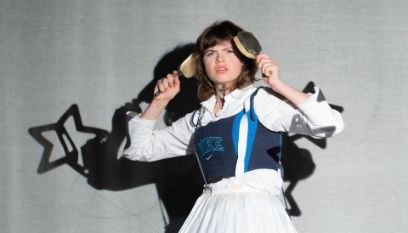 Schauspielerin in dekonstruiertem Dirndl schaut ins Licht, während sie sich die Haare kämmt