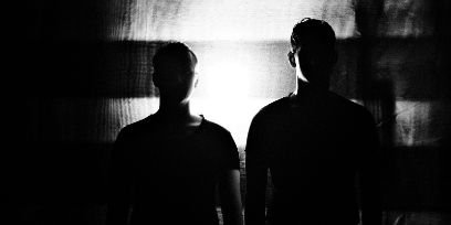 Schwarz-Weiss-Fotografie zweier Männer im Gegenlicht