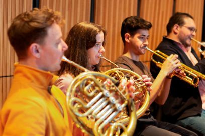 Von links nach rechts spielen ein Hornist, eine Hornistin und zwei Trompeter auf ihren Instrumenten.