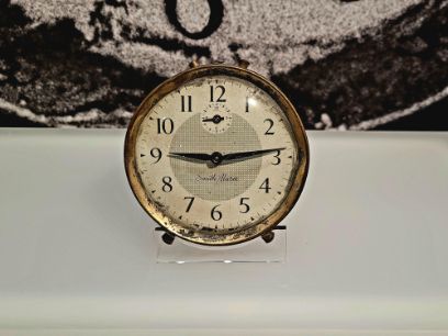 Auf einer weissen gläsernen Oberfläche steht eine weckerähnliche analoge Uhr.