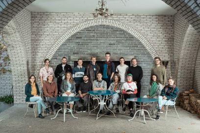 Eine Gruppe von Mitgliedern des jungen Jazz Orchester sitzen und stehen an Tischen und schauen in die Kamera.