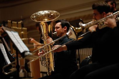 Ein Mann steht mit einem Baritonhorn auf der Büne und spielt. Im Vordergrund steht ein Mann mit einer Posaune.