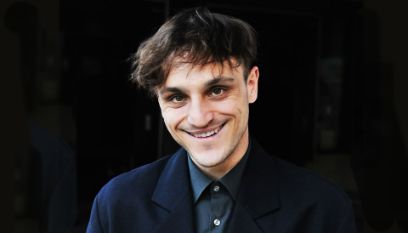 Der Schauspieler Franz Rogowski grinst vor schwarzem Hintergrund schelmisch in die Kamera