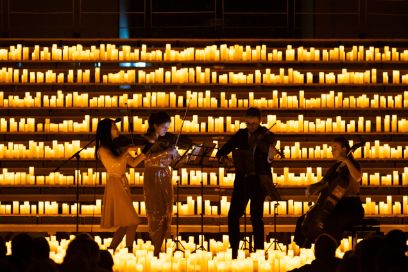 Von links nach rechts zwei Violistinnen und ein Bratschist (stehend) und eine Cellistin (sitzend) vor einem Regal mit brennenden Kerzen.