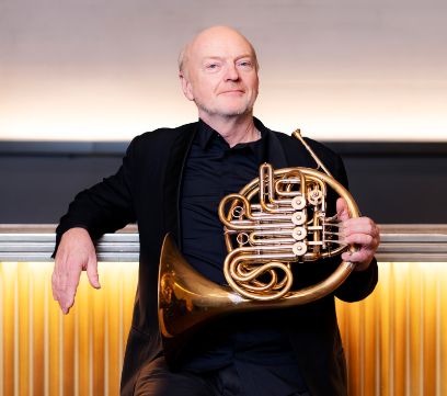 Ein schwarz gekleideter Mann lehnt sich rücklings gegen eine Brüstung, in der linken Hand hält er ein Horn.