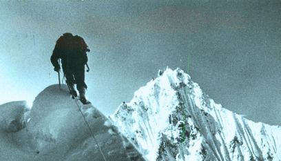 Schemen eines Bergsteigers, der grade den Gipfel erklimmt vor weiss-blauer Bergkulisse