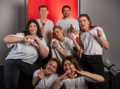 Menschen in weissem Shirt vor einer roten Leinwand machen Herz Symbole mit ihren Fingern