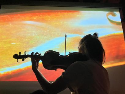 Eine Frau spielt Geige vor einem Bild in rot-orangen Farbtönen.