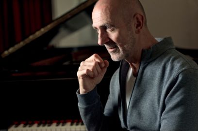 Profilaufnahme eines Mannes, der den rechten Arm aufgestützt vor einem Flügel sitzt.