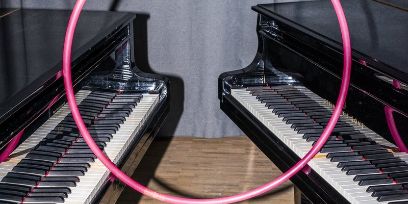 Zwei Flügel stehen mit wenig Abstand Tastatur an Tastatur, abgestützt auf die Tastaturen steht ein Reif.