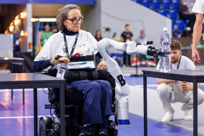 Gabriela Pozzi hebt mit Hilfe des Roboterarms die Flasche vom Boden auf den Tisch am Cybathlon 2024
