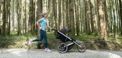 Frau joggt mit Kinderwagen durch den Wald.