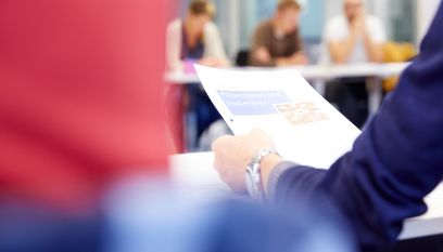 Person studiert Unterlagen, unscharfe Personen im Hintergrund